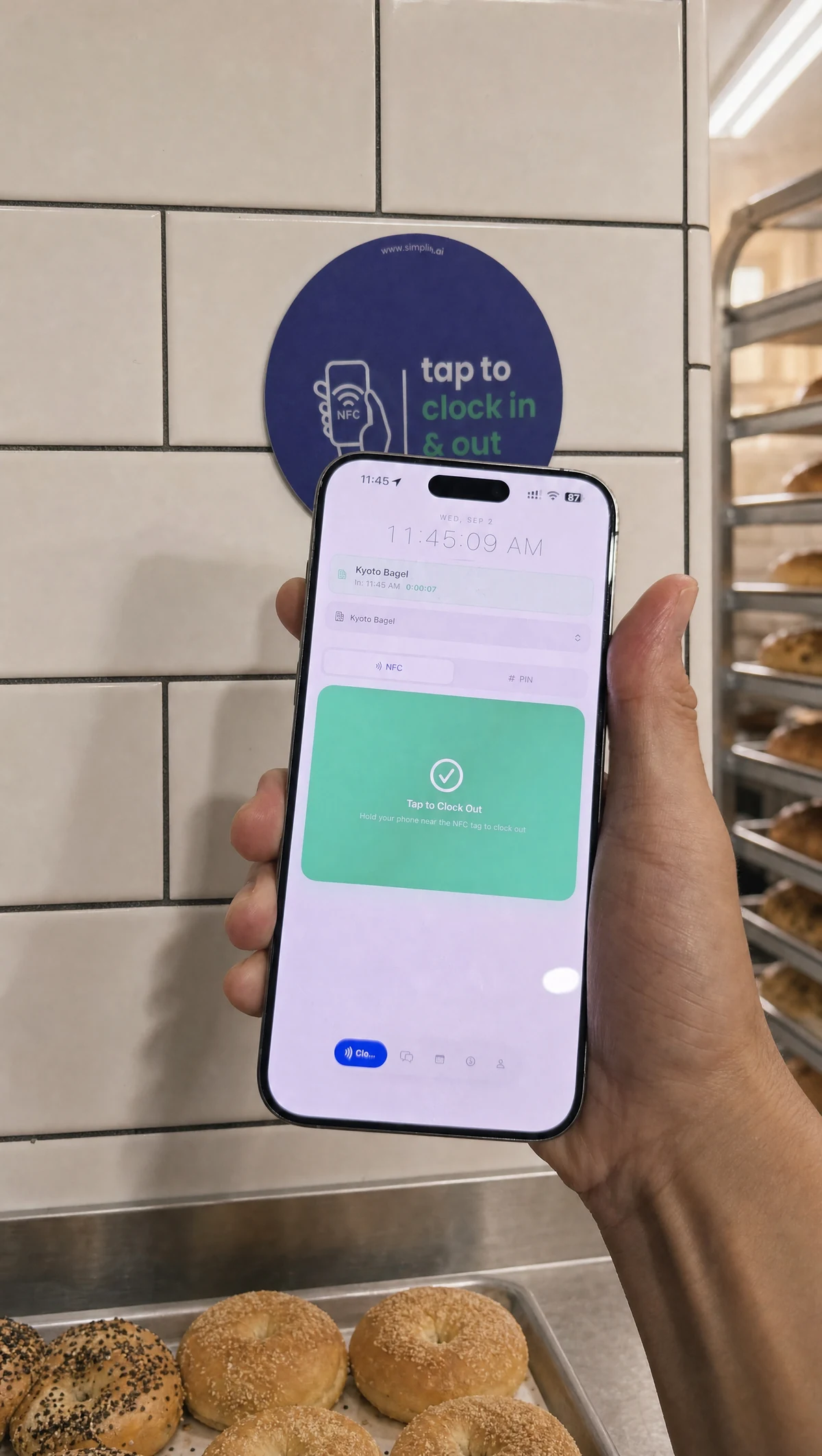 An employee holding the Simplin app next to the NFC sticker on a bagel shop wall